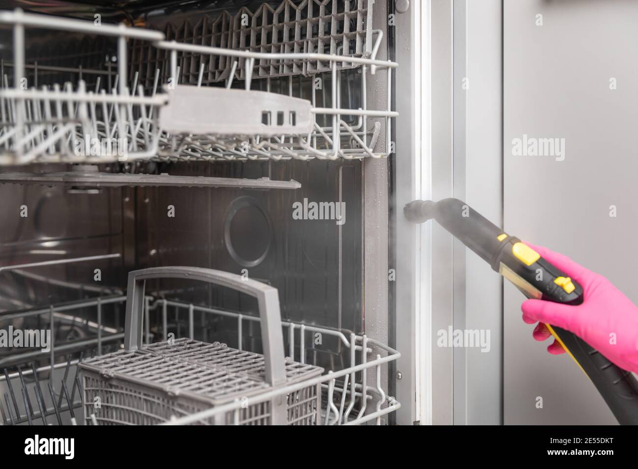 Frauen in Gummihandschuhen reinigen Geschirrspüler mit einem heißen Dampfreiniger. Frühjahrsputz Stockfoto