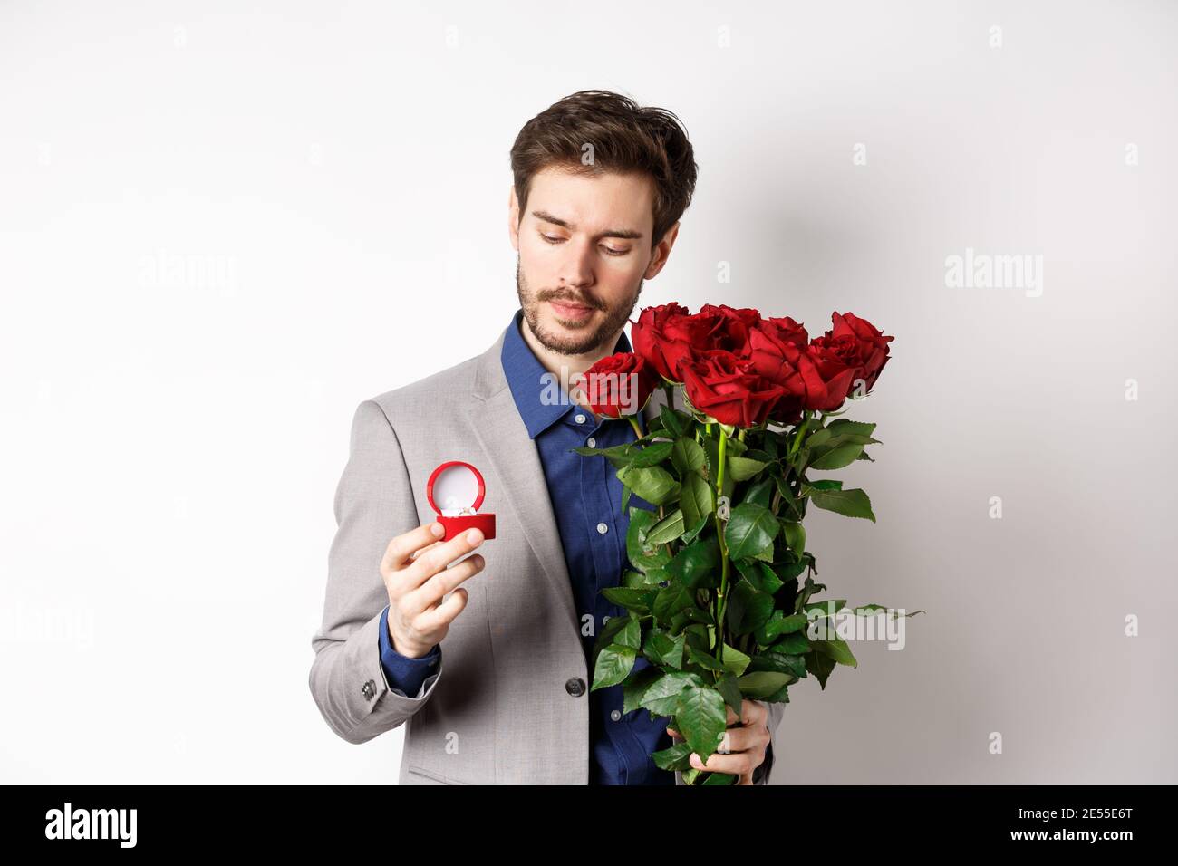Romantischer Mann in Anzug, der nachdenklich am Verlobungsring aussieht,  einen Heiratsantrag am Valentinstag macht, Strauß Rosen hält, über dem er  steht Stockfotografie - Alamy