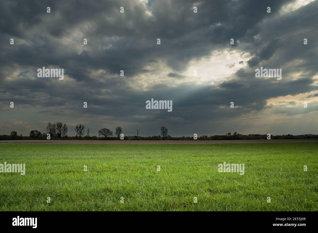 Sonnenlicht, das durch ein Loch in den Wolken auf eine grüne Wiese, Frühlingslandschaft Stockfoto