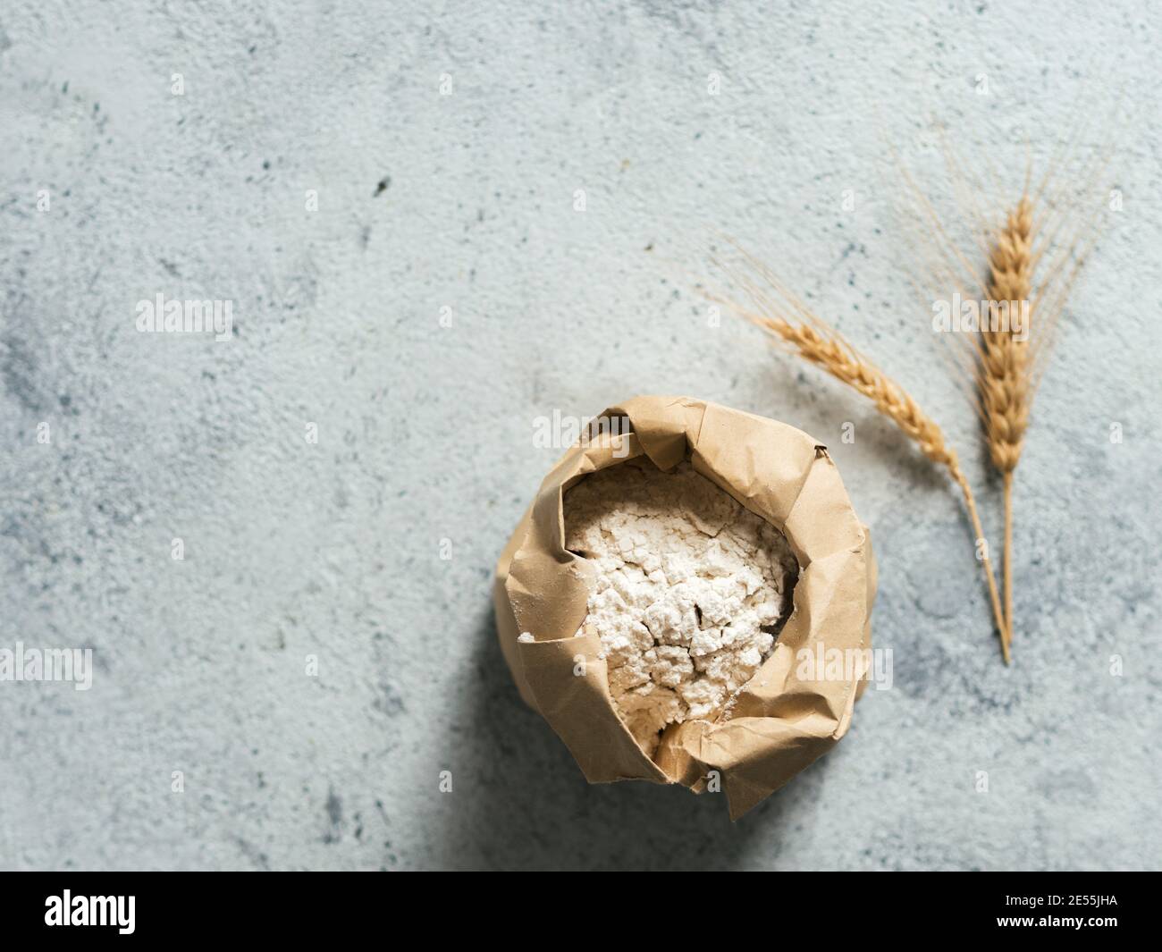 Weizenmehl in Papiertüte und Spikes über grauem Zement Hintergrund. Lebensmittel und Backzutat - Allzweckmehl mit Kopierfläche Stockfoto