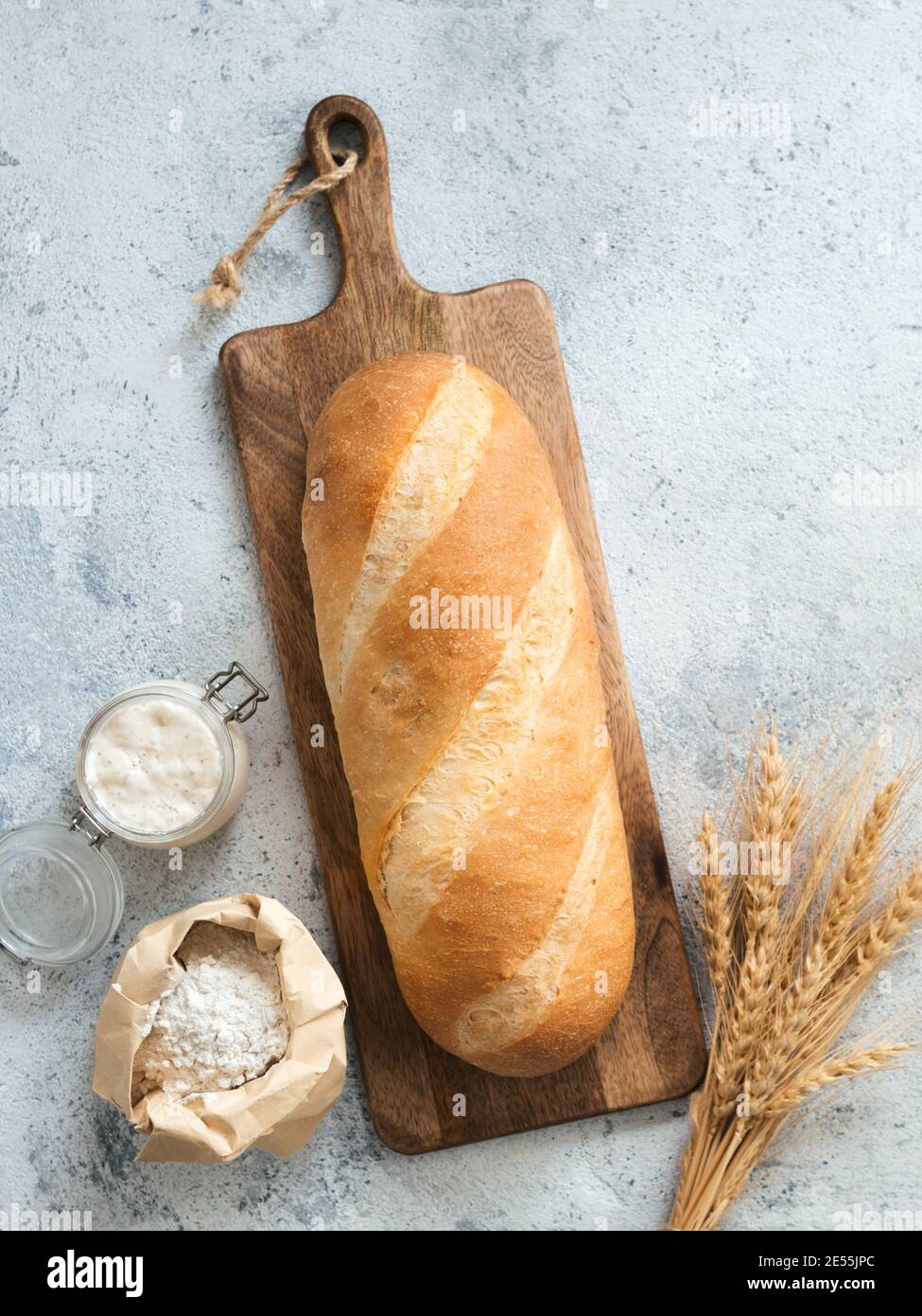 British White Bloomer oder europäischen Sauerteig Baton Laib Brot auf grauem Zement Hintergrund. Frisches Brot, Glas mit Sauerteig Starter, Mehl in Papiertüte und Ohren. Draufsicht. Speicherplatz kopieren. Vertikal Stockfoto