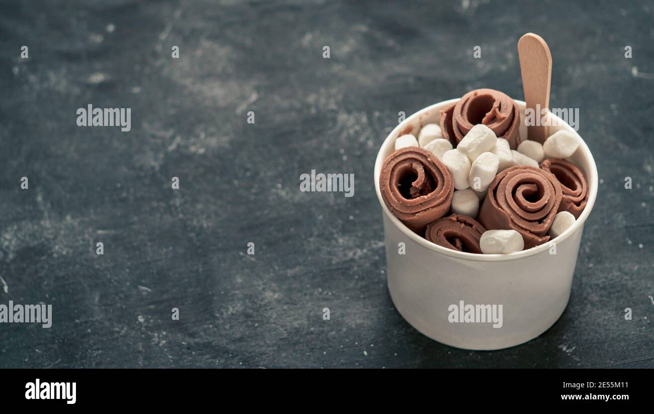 Gerolltes Eis mit in-Cone-Tasse auf dunklem rustikalem Hintergrund. Iced Rolls mit Schokolade. Thailändisches Schokoladeneis mit Rollen und Platz für Text oder Design. Banner. Tageslicht Stockfoto