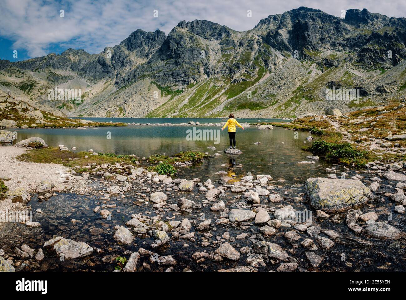 Wanderer Frau erkunden Sie die fantastische Landschaft und genießen Sie die Aussicht in der Nähe eines Bergsees in gelb in Jacke, hohe Tatra, Slowakei Stockfoto