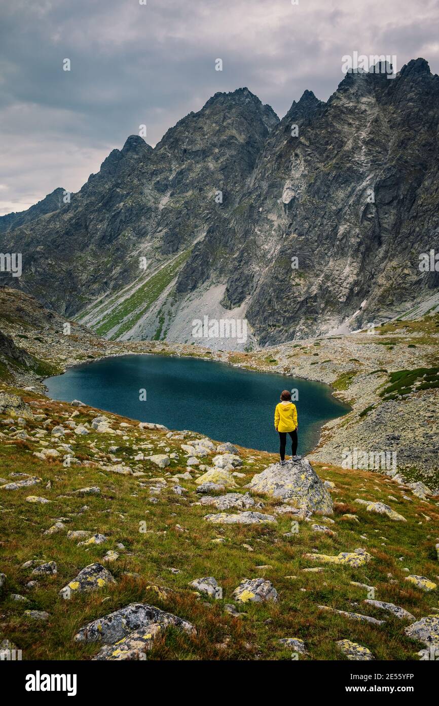 Wanderer Frau erkunden Sie die fantastische Landschaft und genießen Sie die Aussicht in der Nähe eines Bergsees in gelb in Jacke, hohe Tatra, Slowakei Stockfoto