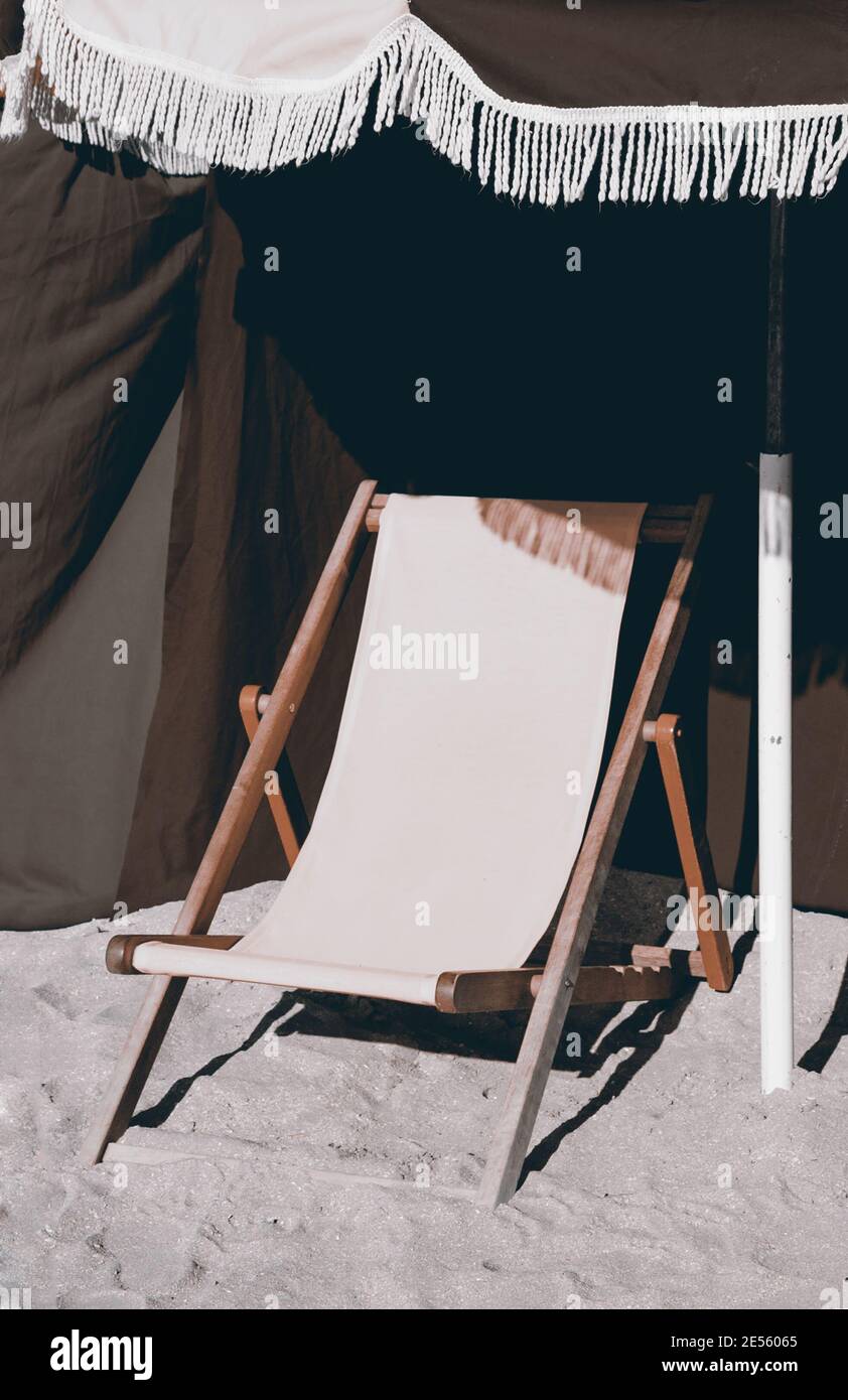 Strandliegen aus Holz und Sonnenschirm mit Fransen. Trouville-sur-Mer (Normandie, Frankreich). Ausgewählte Fokussierung auf den Rand. Foto in Retro-Farben. Stockfoto