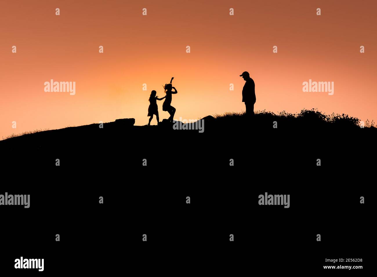Ein Erwachsener und zwei Kinder auf dem Pentire Point East, der von einem intensiven, farbenfrohen Sonnenuntergang in Newquay in Cornwall umgeben ist. Stockfoto
