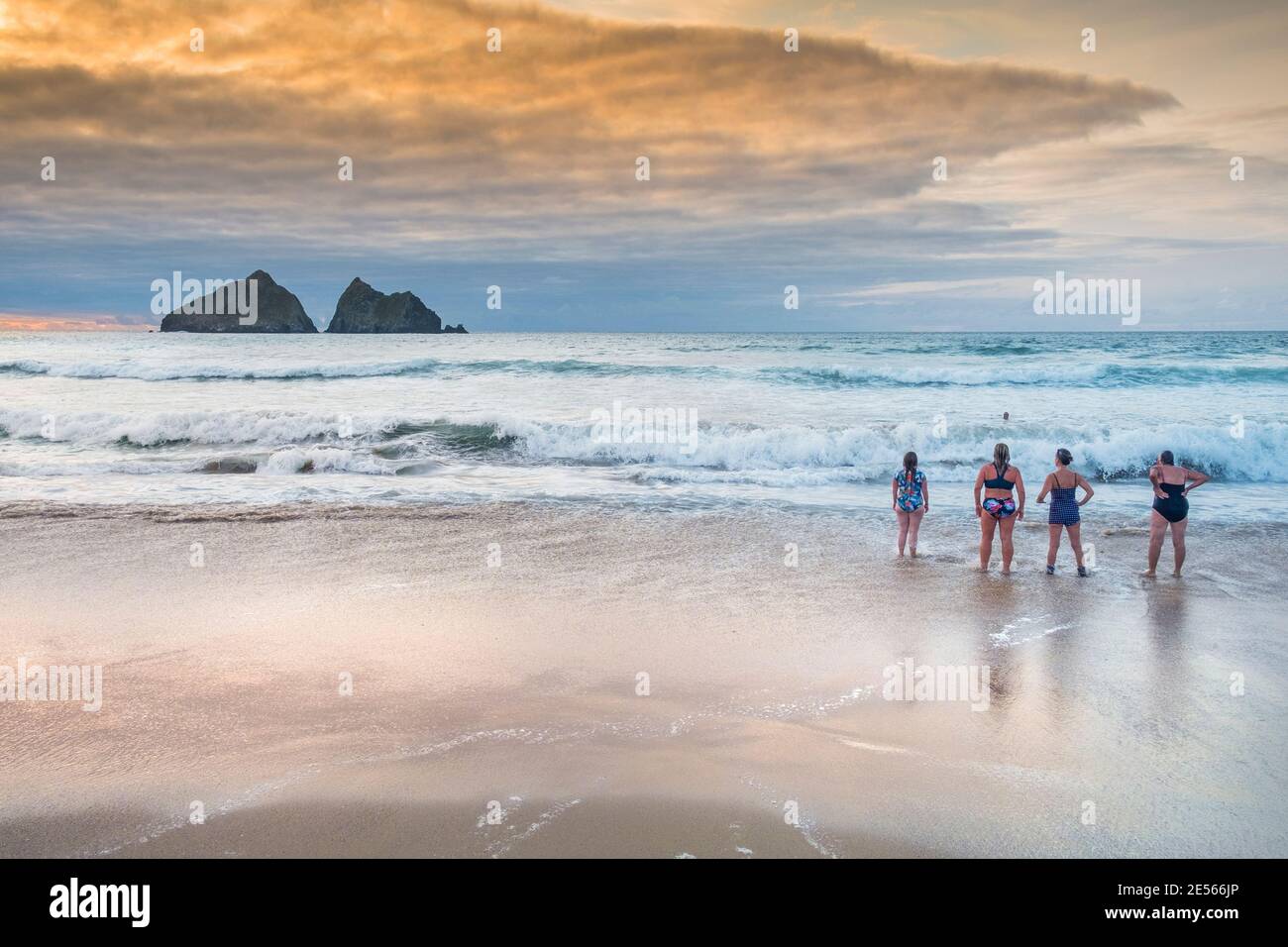 Schwimmerinnen stehen an der Küste am Holywell Beach mit Gull Rocks in der Ferne in Cornwall. Stockfoto