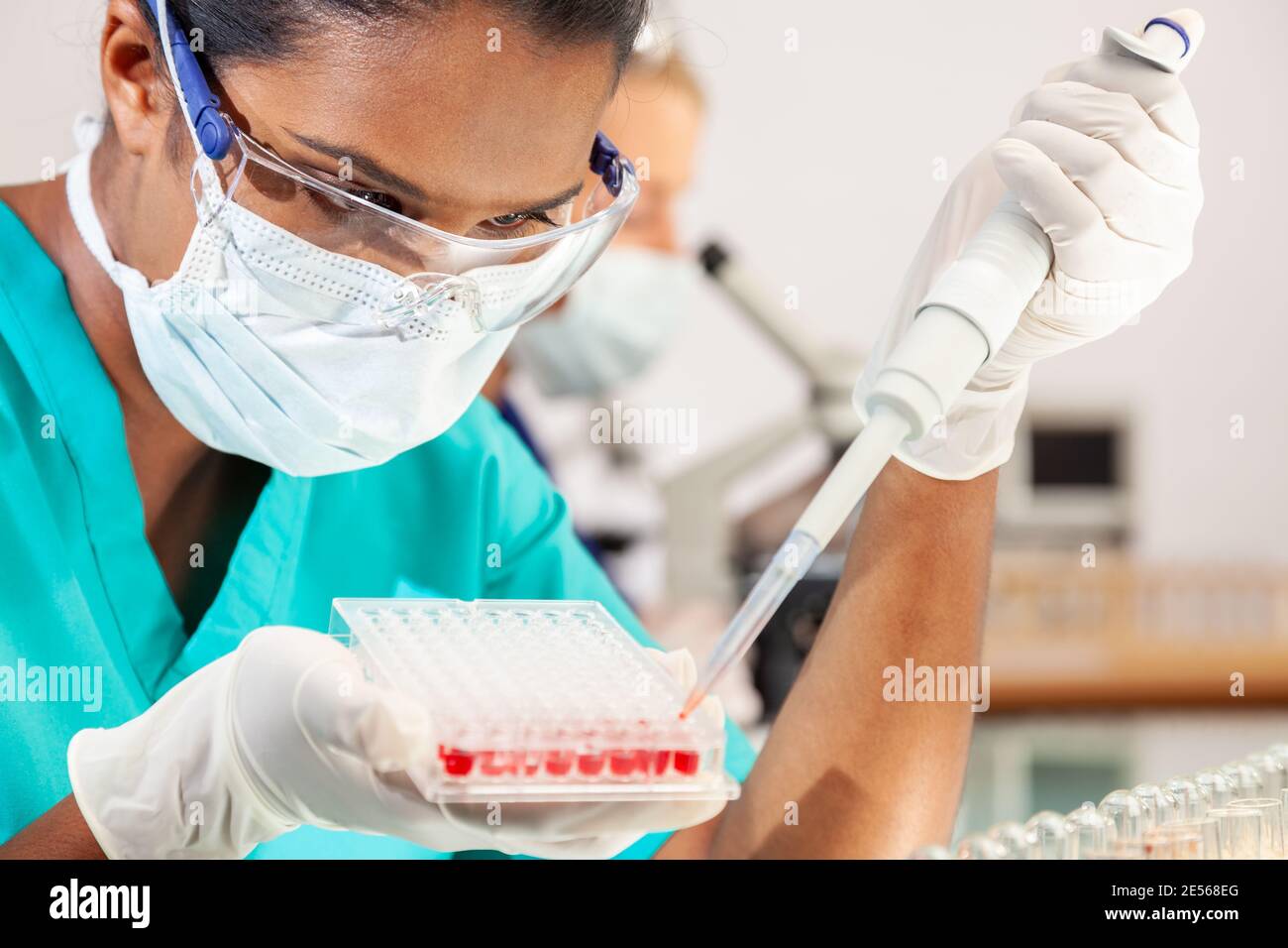 Weibliche asiatische medizinische oder wissenschaftliche Forscher oder Arzt trägt Gesicht Maske mit Probenteller mit Blutproben im Labor Mit ihrem blonden weiblichen coll Stockfoto