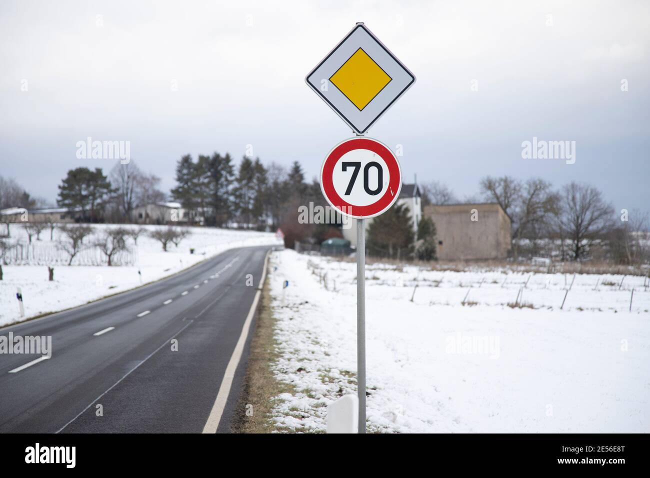 Landstraße im Winter, Schnee auf dem Boden, Tempolimitschild 70 kmh und ein Wegweiser Stockfoto
