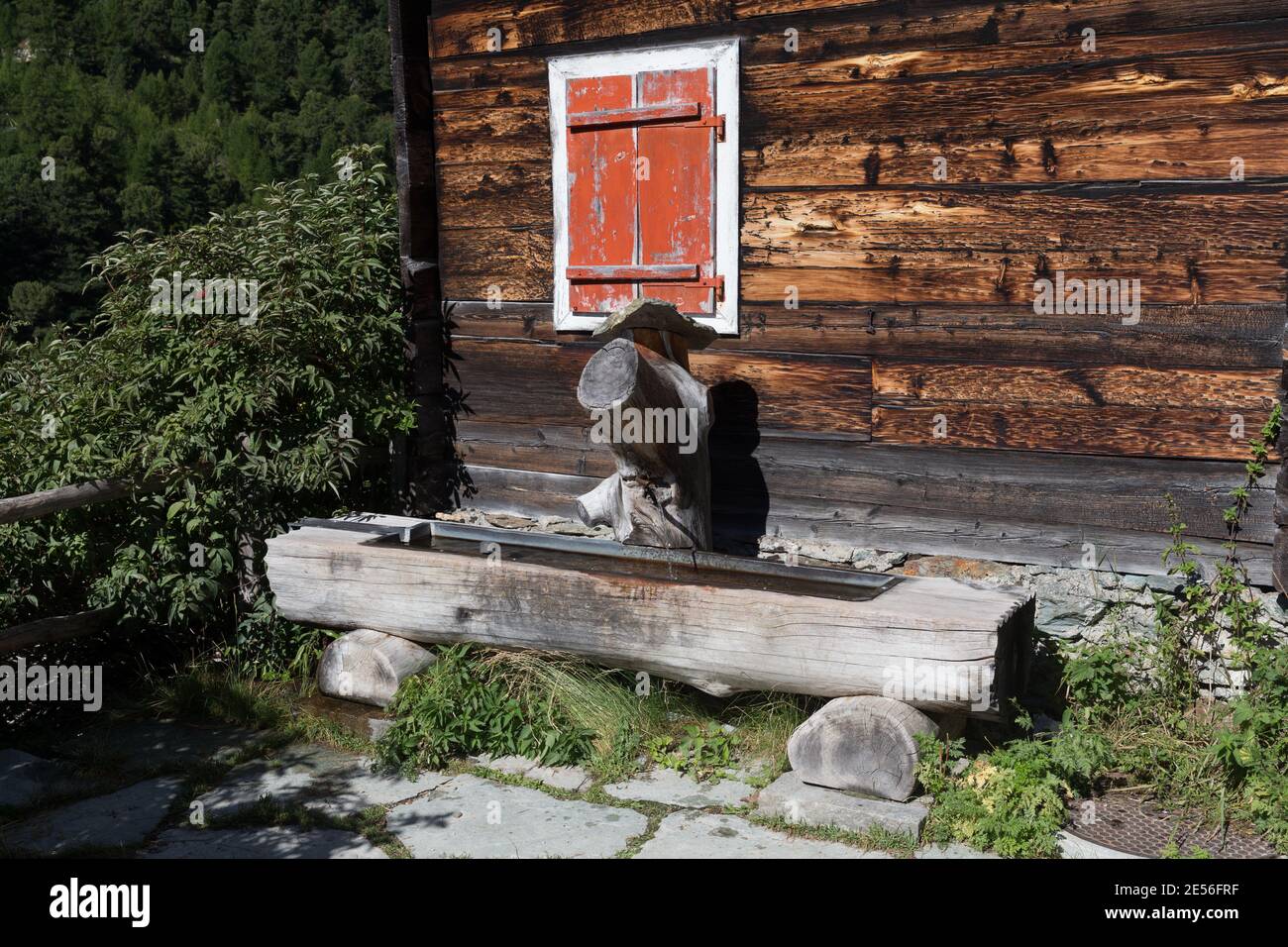 Schweiz Ein traditioneller Holzbrunnen neben einem alten Holzhaus im Alpendorf Zmutt. Stockfoto