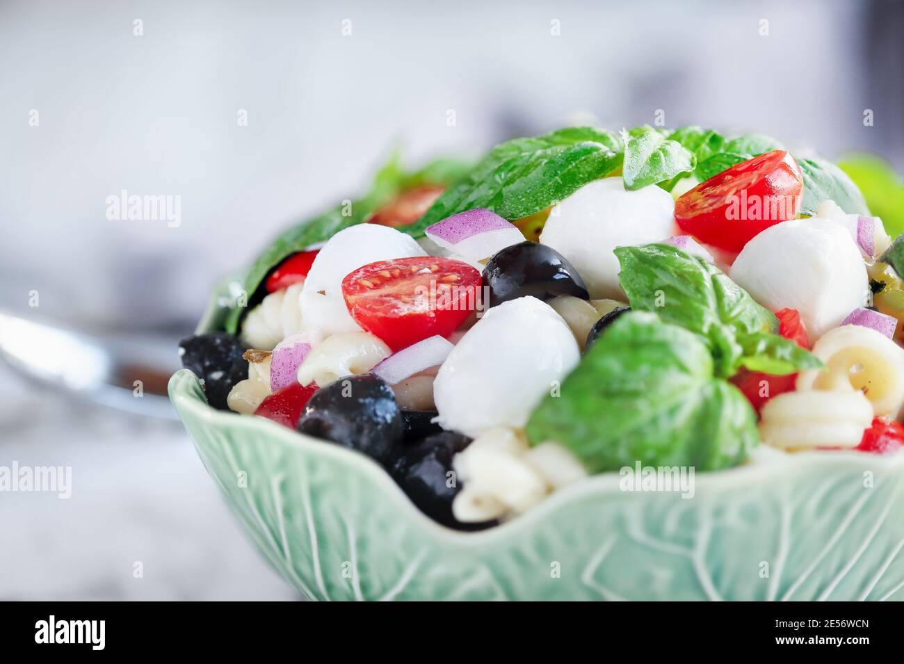 Italienischer Nudelsalat mit frischen Tomaten, schwarzen Oliven, roten Zwiebel Mozzarella Käsebällchen, Basilikum und einem Olivenöl-Dressing. Extrem selektiver Fokus wi Stockfoto