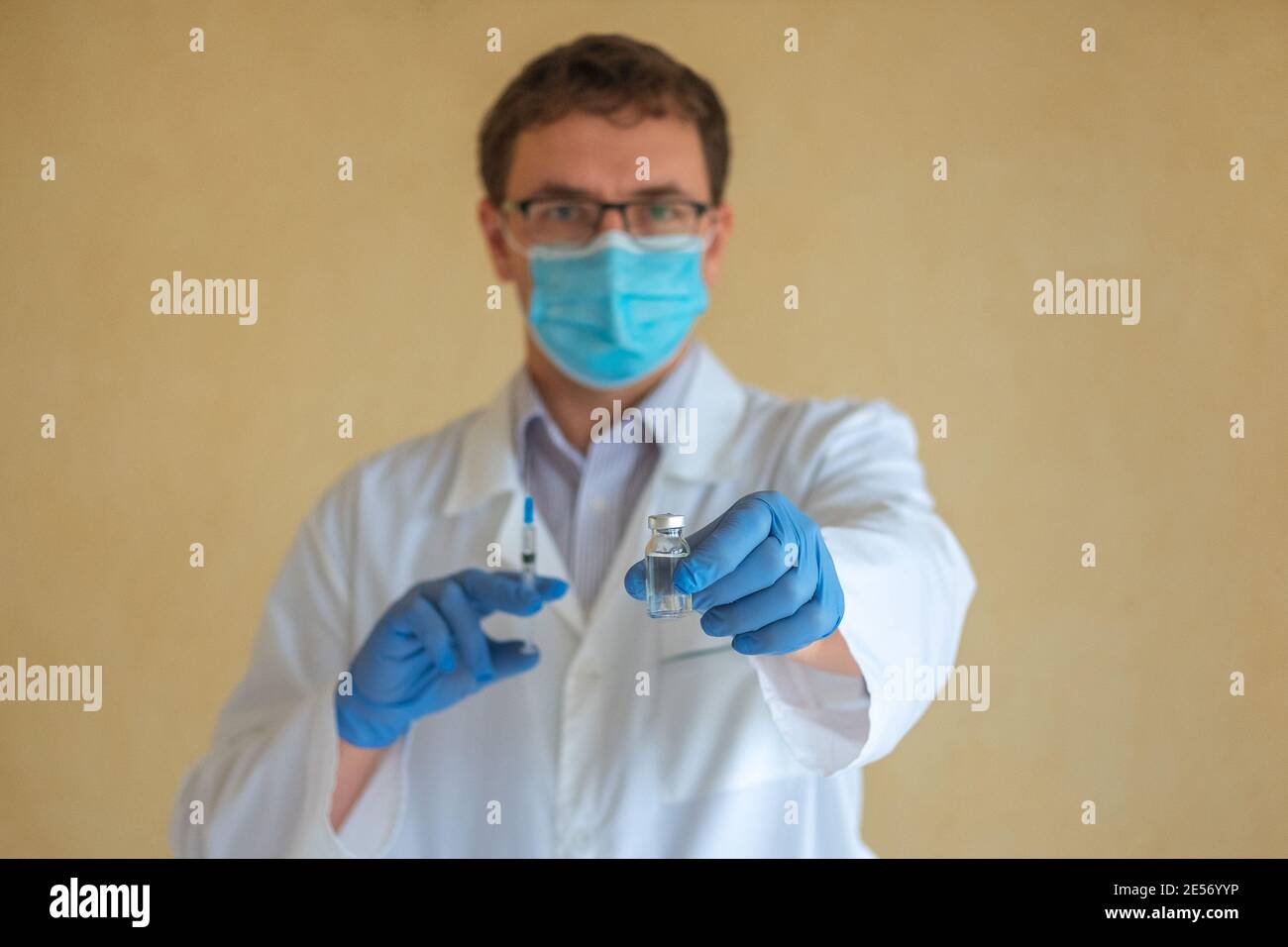 Ein Mann Arzt in einer Schutzmaske und blauen Latexhandschuhen hält eine Ampulle mit einem Impfstoff und einer Spritze. Konzentrieren Sie sich auf die Ampulle Stockfoto