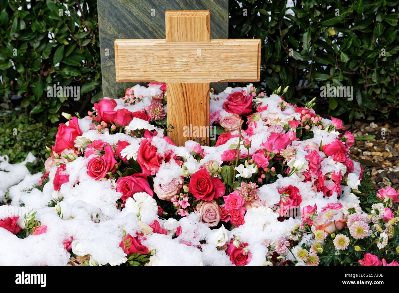 Schneebedeckte Blumendekoration aus Rosen bei einem Grab mit Holzkreuz Stockfoto