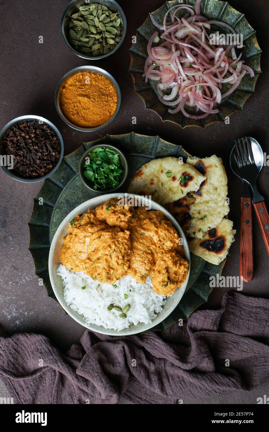 Indisches Butter-Huhn mit Basmati-Reis, Gewürze, Naan-Brot. Zwiebelsalat, Brauner Hintergrund. Leerzeichen für Text Stockfoto