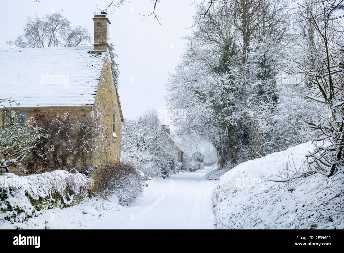 Landstraße und cotswold Steinhütten in Swinbrook im Schnee. Swinbrook, Cotswolds, Oxfordshire, England Stockfoto