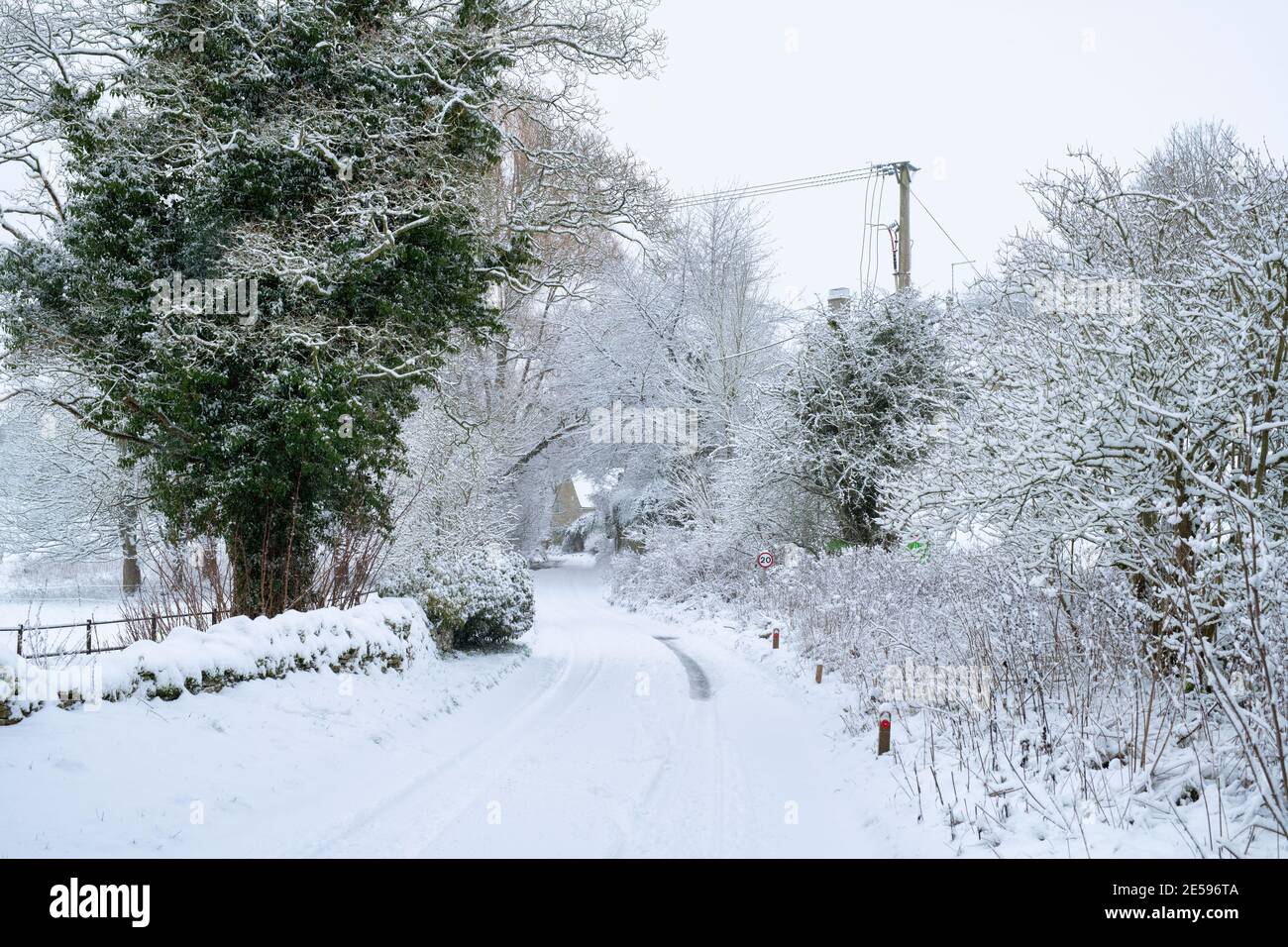 Landstraße und Bäume in Swinbrook im Schnee. Swinbrook, Cotswolds, Oxfordshire, England Stockfoto