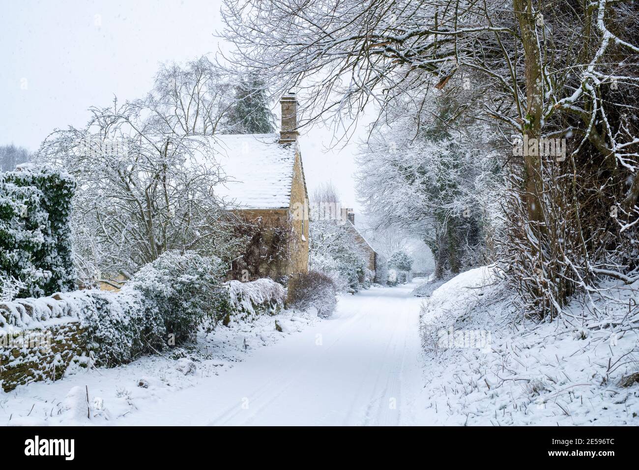 Landstraße und cotswold Steinhütten in Swinbrook im Schnee. Swinbrook, Cotswolds, Oxfordshire, England Stockfoto