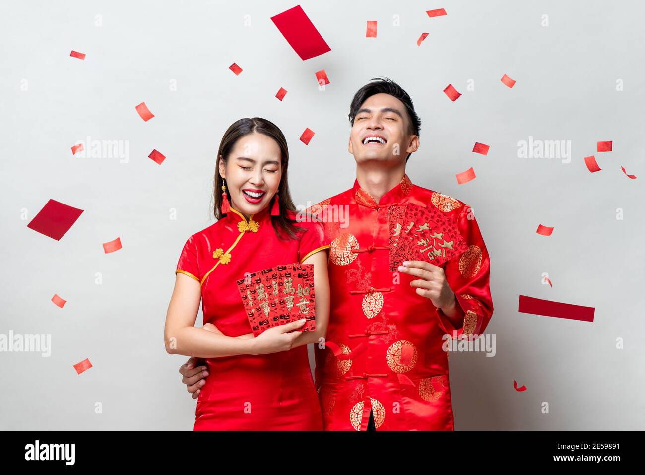 Glückliches asiatisches Paar in traditionellen orientalischen Kostümen mit roten Umschlägen oder Ang Pao auf hellgrauem Hintergrund für chinesische Neujahrskonzepte, textet mir Stockfoto