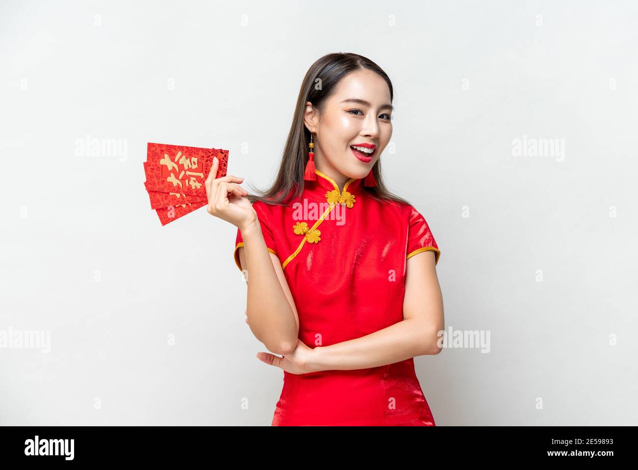 Lächelnde asiatische Frau im orientalischen Cheongsam Kostüm präsentiert rote Umschläge Oder Ang Pao isoliert auf hellgrauem Studiohintergrund für Chinesisches Neujahr CO Stockfoto