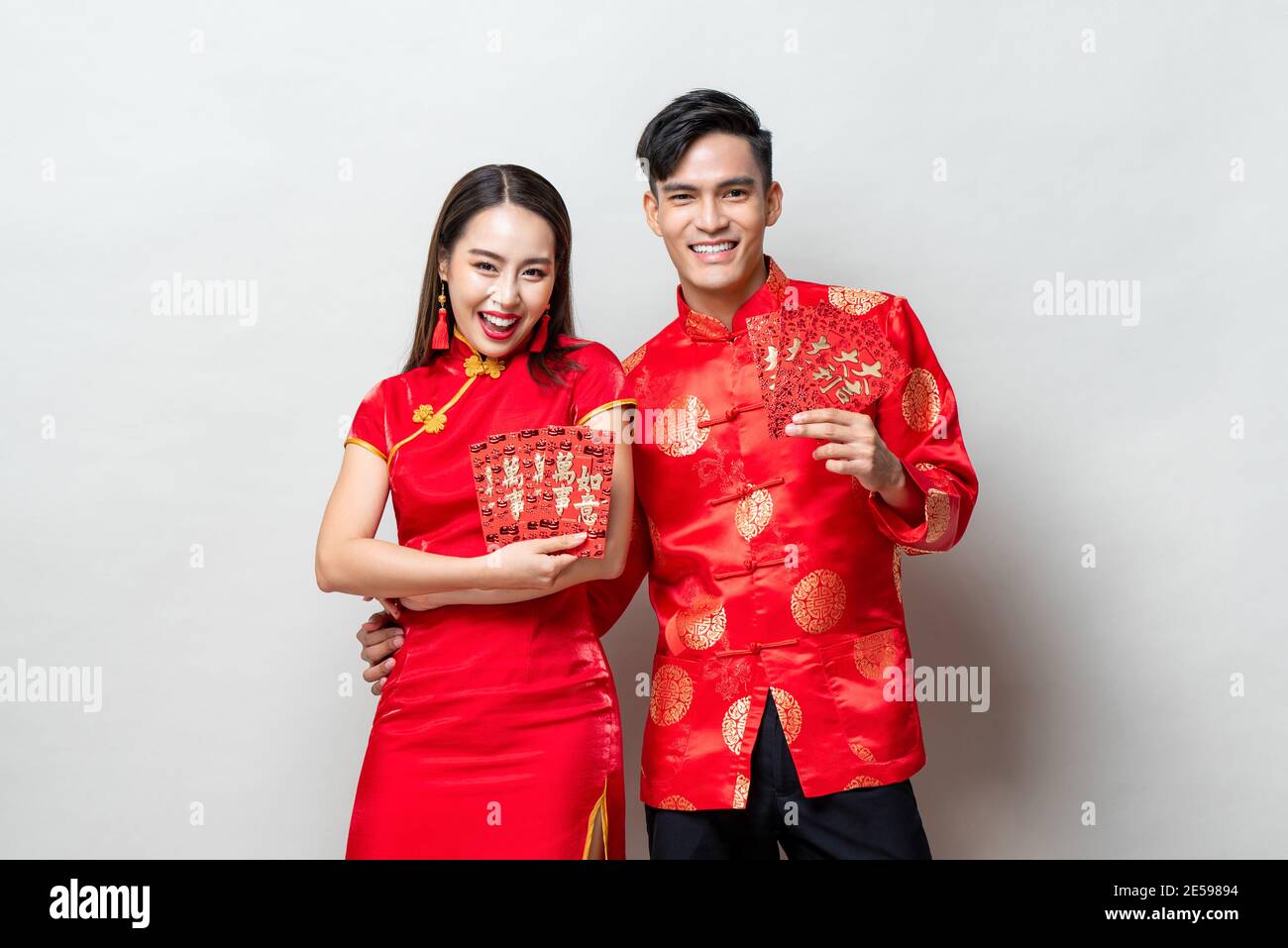 Glückliches asiatisches Paar in traditionellen orientalischen Kostümen mit roten Umschlägen oder Ang Pao auf hellgrauem Hintergrund für chinesische Neujahrskonzepte, textet mir Stockfoto
