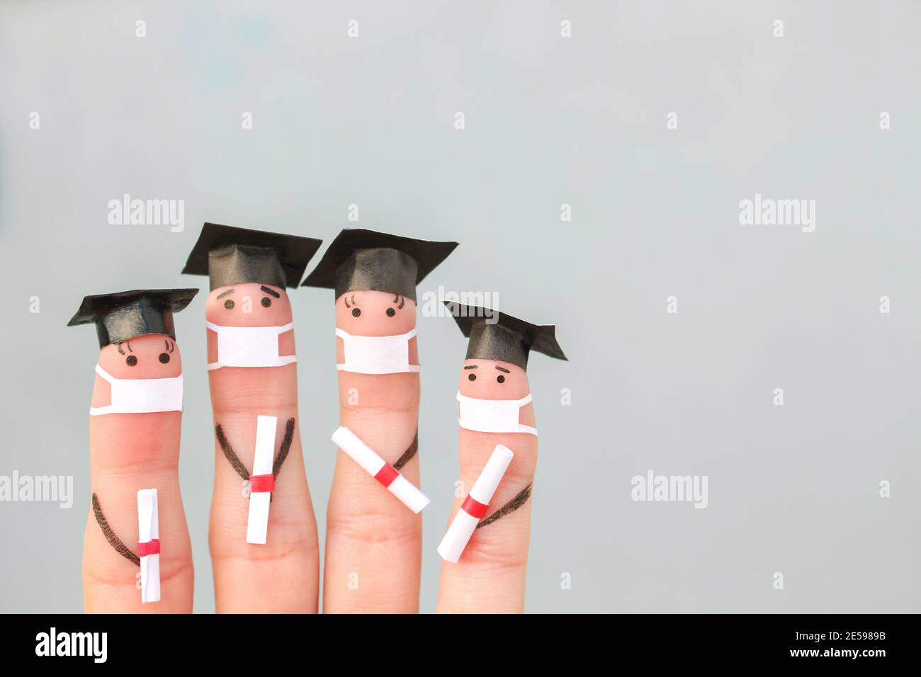 Finger Kunst von Studenten in medizinische Maske aus COVID-2019. Absolventen, die ihr Diplom nach dem Abschluss halten. Stockfoto