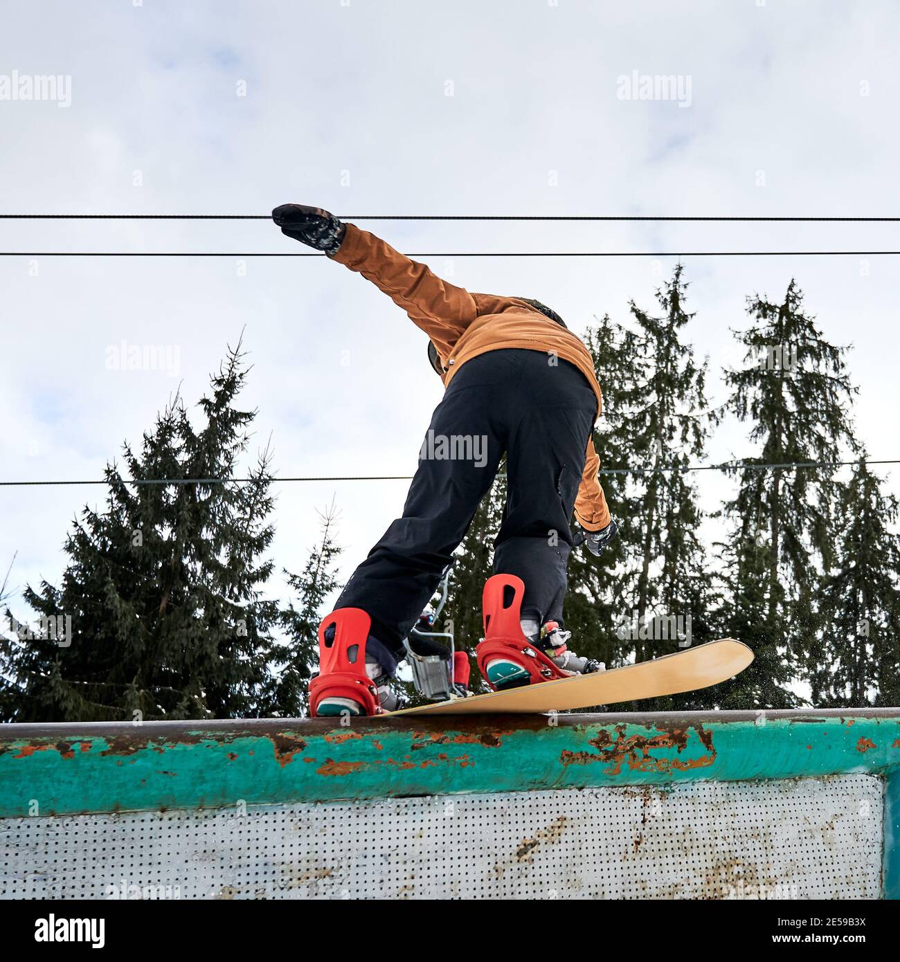Rückansicht des gebeugten Snowboarders, der versucht, Balance zu halten, niedrige Winkelansicht. Sportler in farbenfrohem, lebhaftem Skianzug, roten Stiefeln und Snowboard. Konzept der Freeride Stockfoto