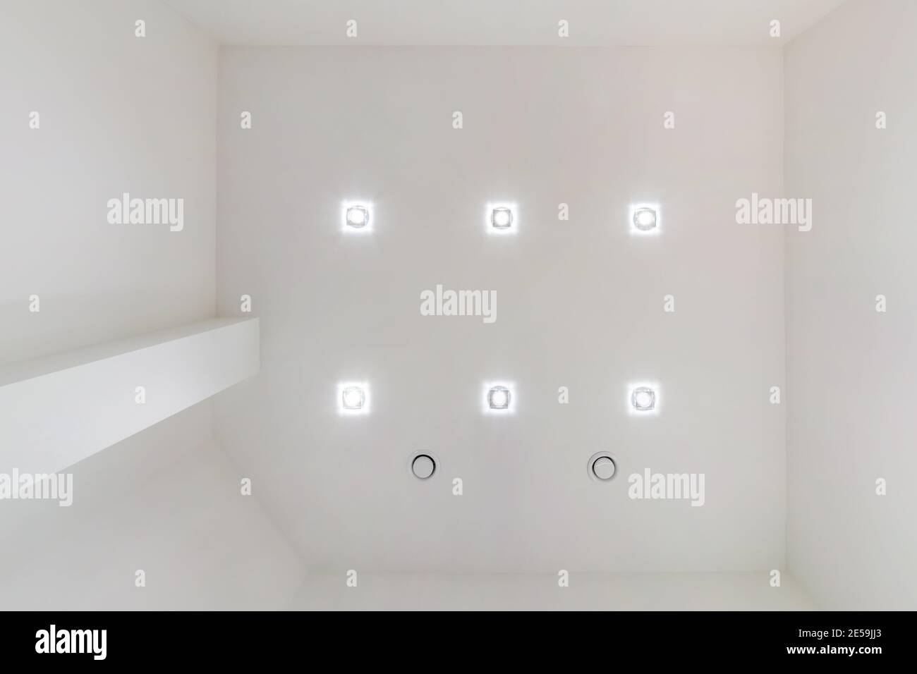 Abgehängte Decke mit Halogenstrahlern und Trockenmauerkonstruktion im leeren Raum in Wohnung oder Haus. Stretchdecke weiß und komplex. Stockfoto