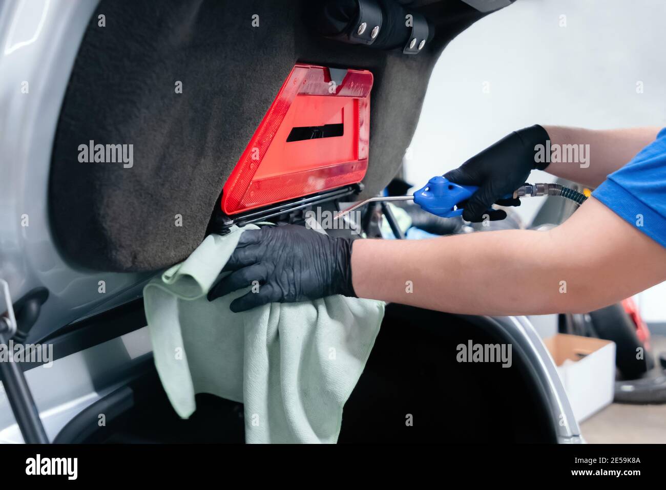 Nahaufnahme des Autowaschers mit Schutzhandschuhen und Reinigung des Kofferraums mit Druckluft und einem Wischtuch Stockfoto