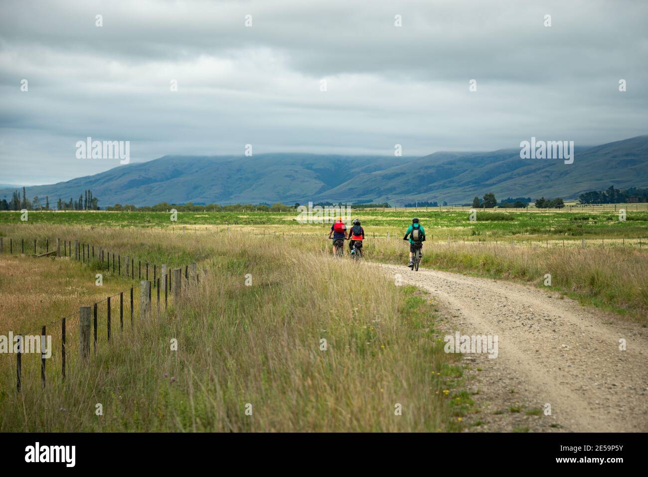 Drei Radfahrer fahren den Otago Central Rail Trail mit schweren Wolken über die Bergketten, South Island Stockfoto