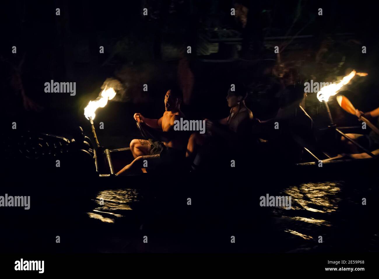 Einige wilde Maori-Krieger paddeln nachts ein uraltes Waka (Kriegerkanu) den Wai-o-whiro-Bach hinunter, Mitai Maori Village, Rotorua, Neuseeland Stockfoto