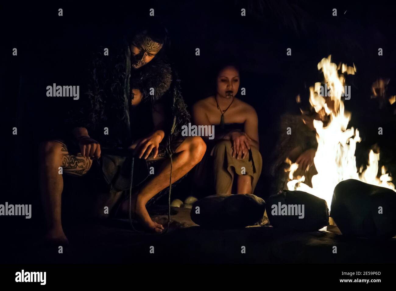 Horizontale Nahaufnahme eines Maori-Paares in traditioneller Kleidung, bei Nacht am Lagerfeuer, Mitai Maori Village, Rotorua, Neuseeland Stockfoto