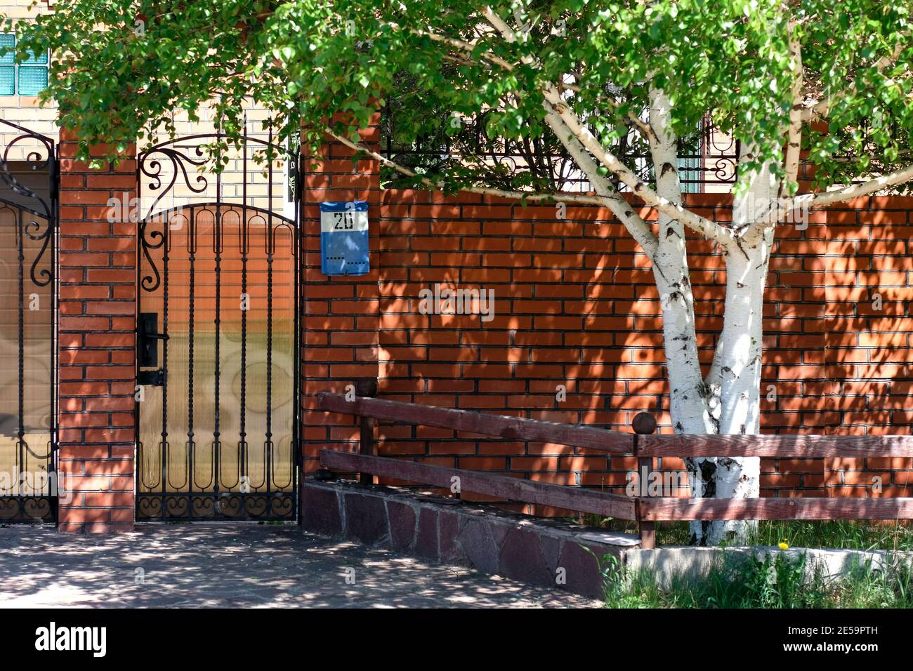 Das Tor zum Haus besteht aus rotem Backstein. Eine blaue Mailbox mit der Nummer 20 ist sichtbar. Birke wächst in der Nähe, Frühling Stockfoto
