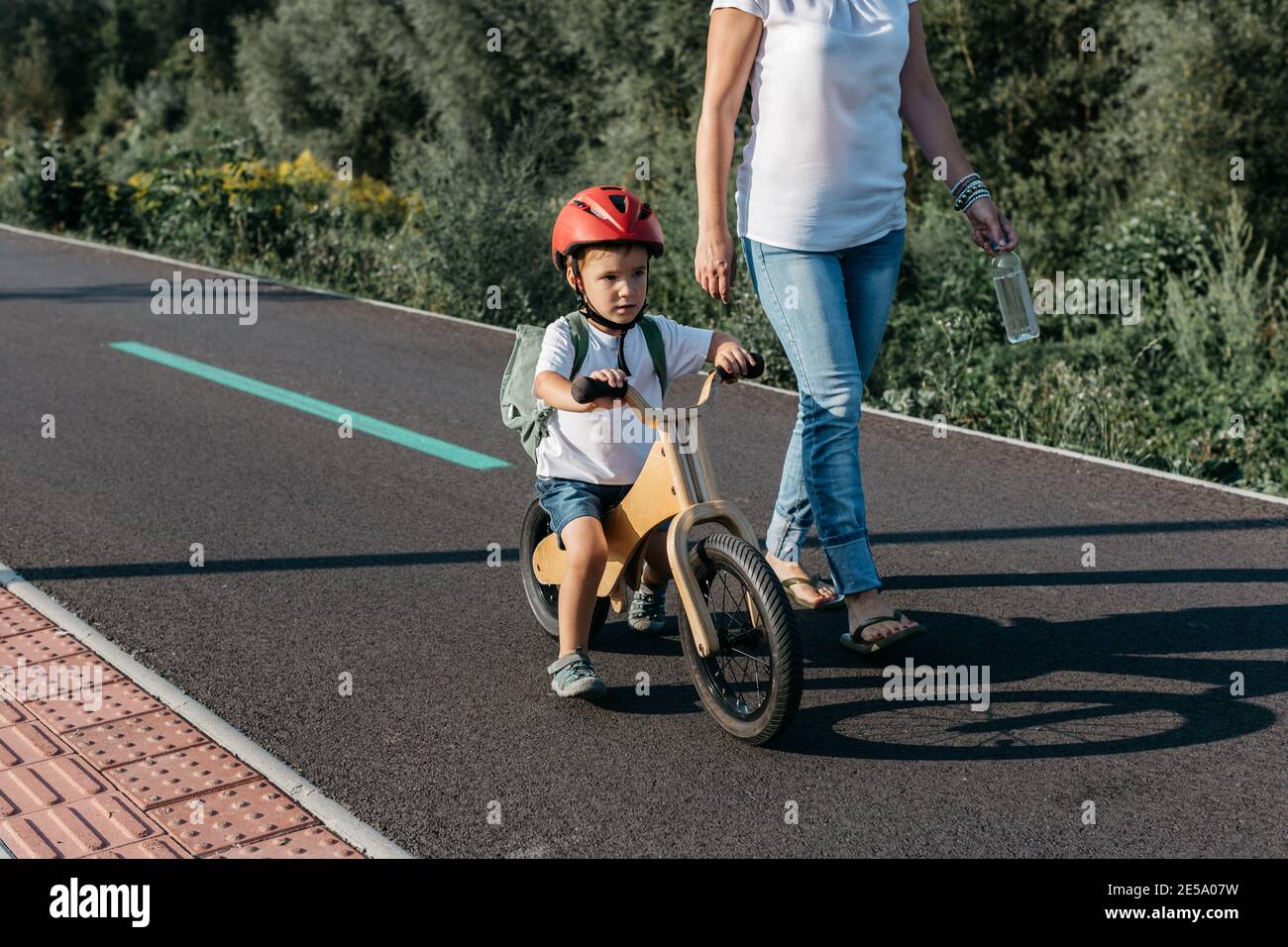 Kind fährt mit dem Laufrad auf einem Fahrradweg. Mutter und Sohn auf dem morgendlichen Schulweg. Stockfoto