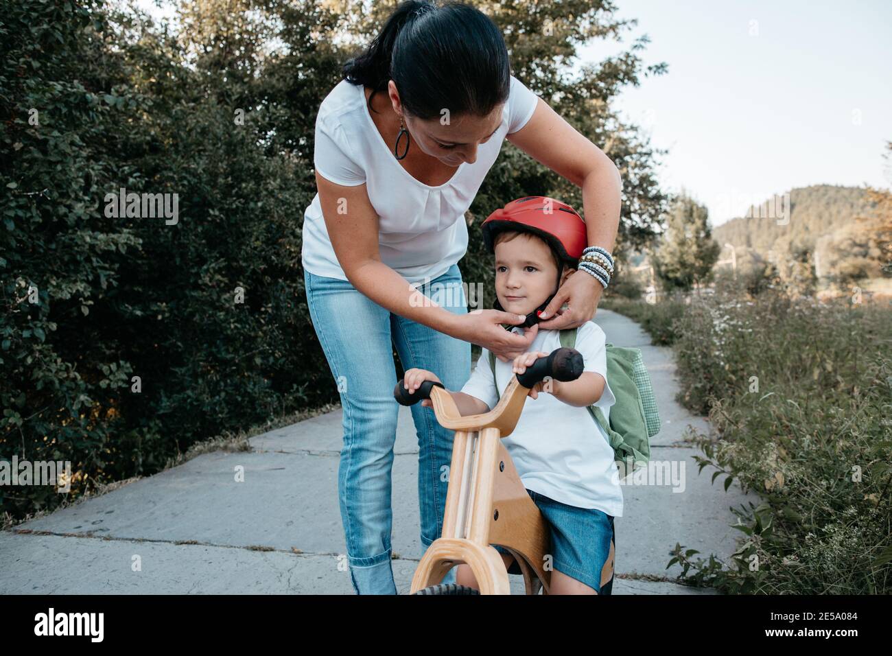 Mutter hilft ihrem kleinen Jungen, einen Fahrradhelm zu befestigen. Frau und Kind auf einem Fahrrad mit Helm. Stockfoto