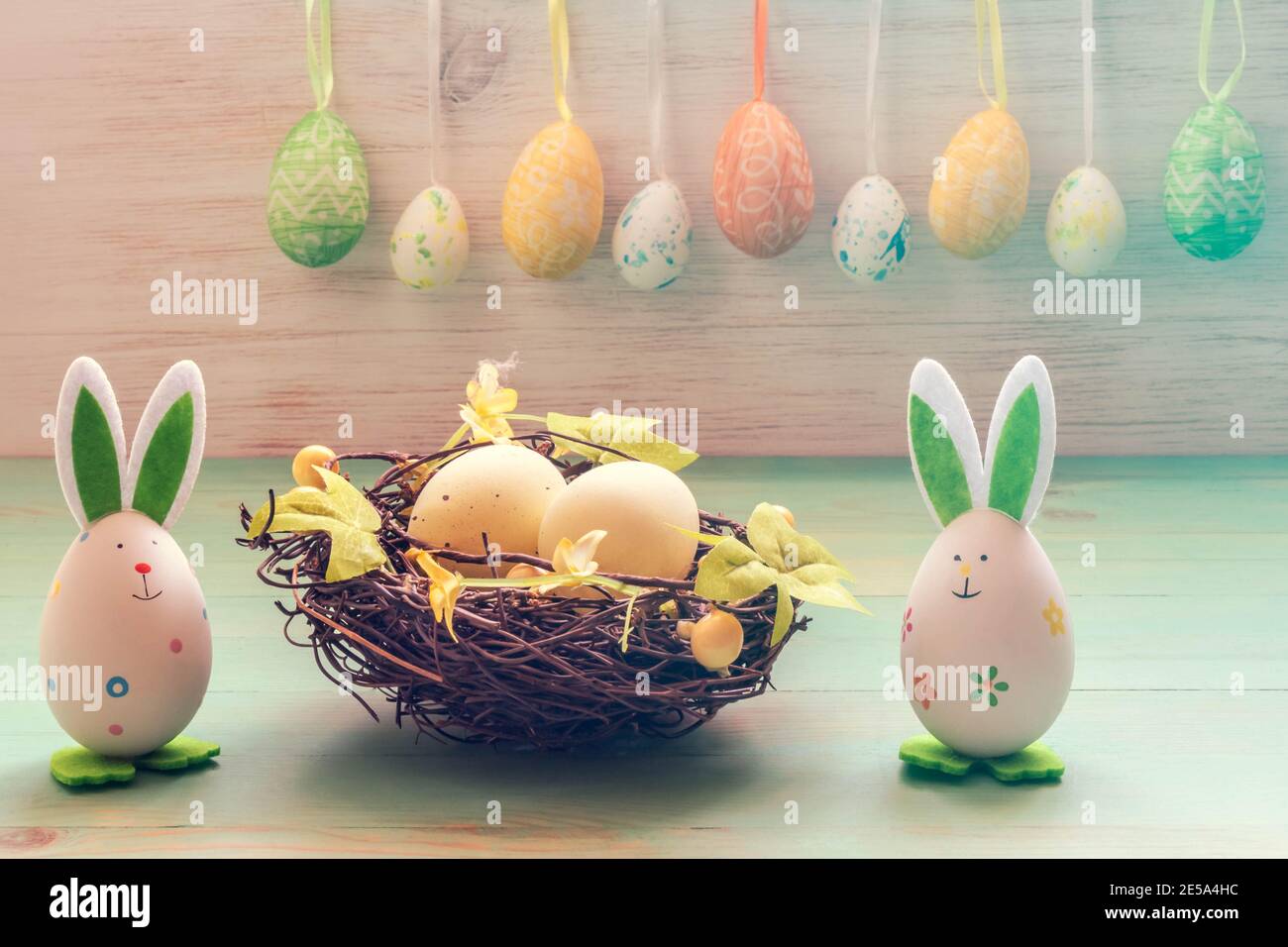 Osterkaninchen Spielzeug, Eier im Nest und Reihe von hängenden Eiern auf Vintage Holz Hintergrund. Osterlaune. Lustige Osterdekoration. Stockfoto