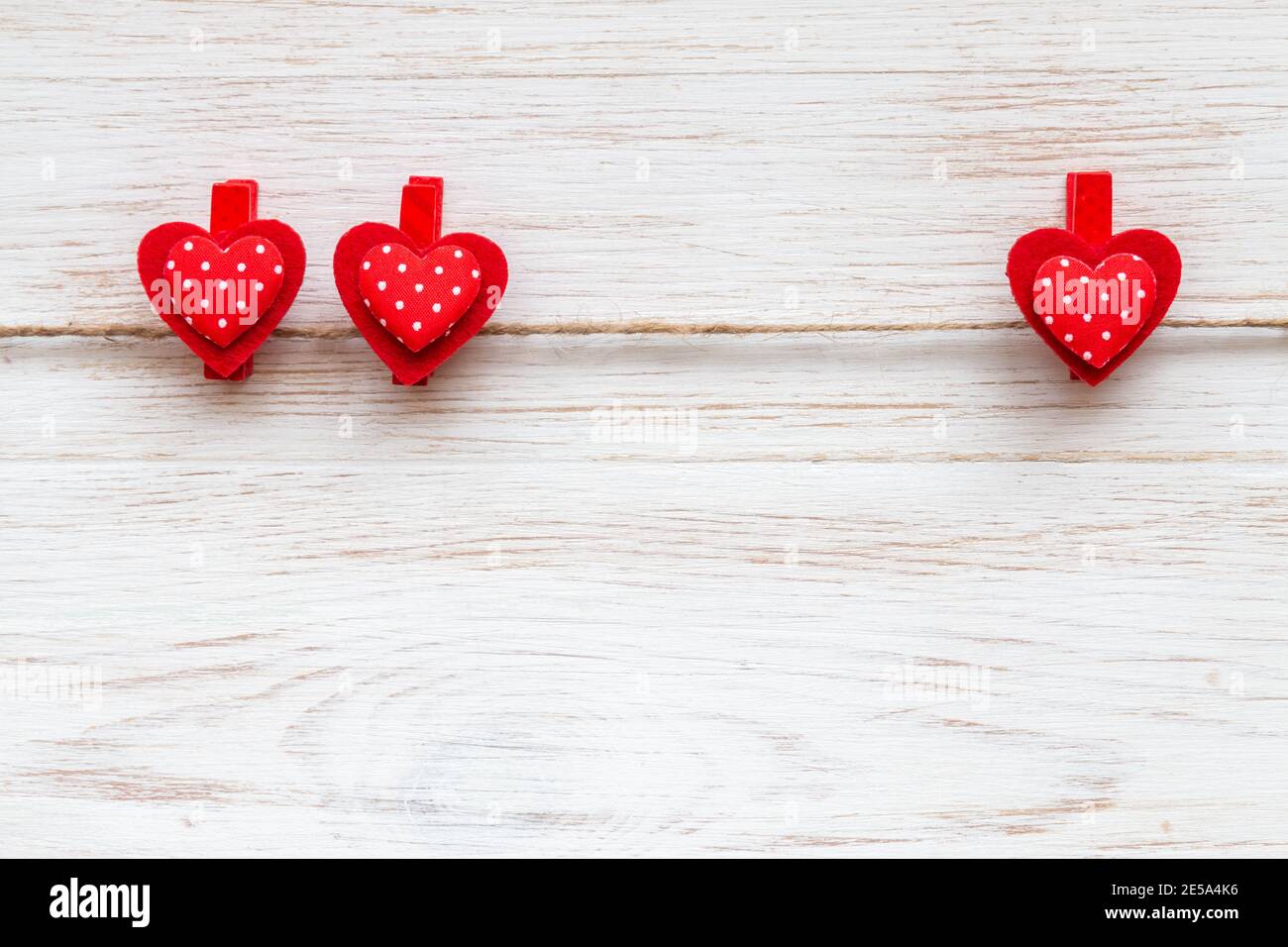 Zwei und ein rote Herzen mit Tupfen auf Wäscheklammern auf rustikal weiß lackiertem Holzbrett. Valentinstag Hintergrund mit roten Herzen. Speicherplatz kopieren Stockfoto