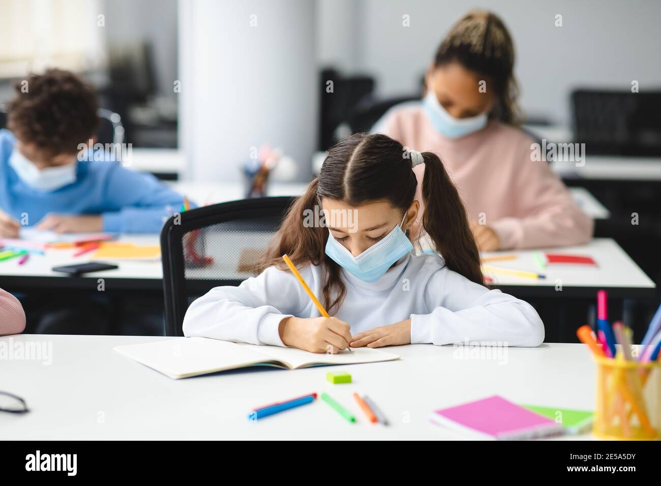 Mädchen in Maske sitzt am Schreibtisch im Klassenzimmer Stockfoto