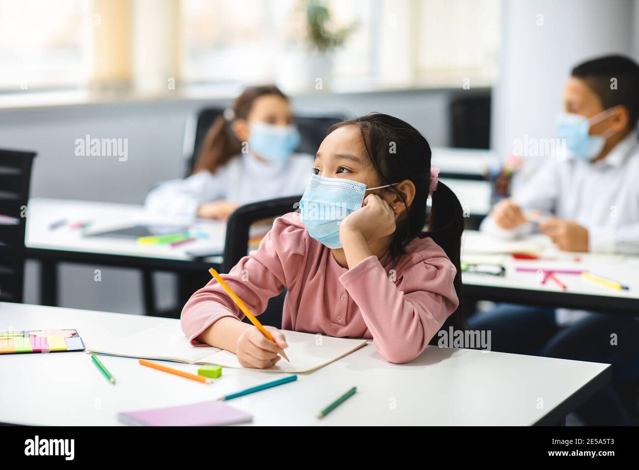 Asiatische Mädchen in Maske sitzen am Schreibtisch im Klassenzimmer Stockfoto