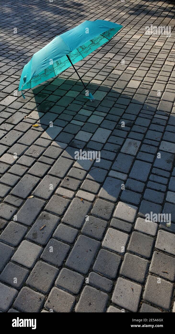 Türkisfarbener Regenschirm auf Steinfliesen, nass nach Regen. Offener blauer Regenschirm mit Kunstdruck in London Tower Bridge Stockfoto