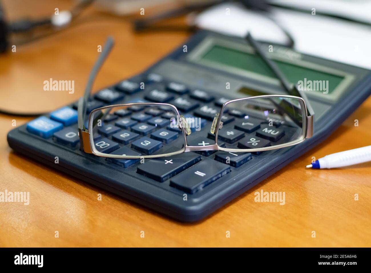 Minimale Brillen auf dem Bürorechner mit Zahlen auf Tasten in Fokus durch Brillengläser und verschwommener Hintergrund von Holztisch Und Unschärfe-Unschärfe-Unschärfe Stockfoto