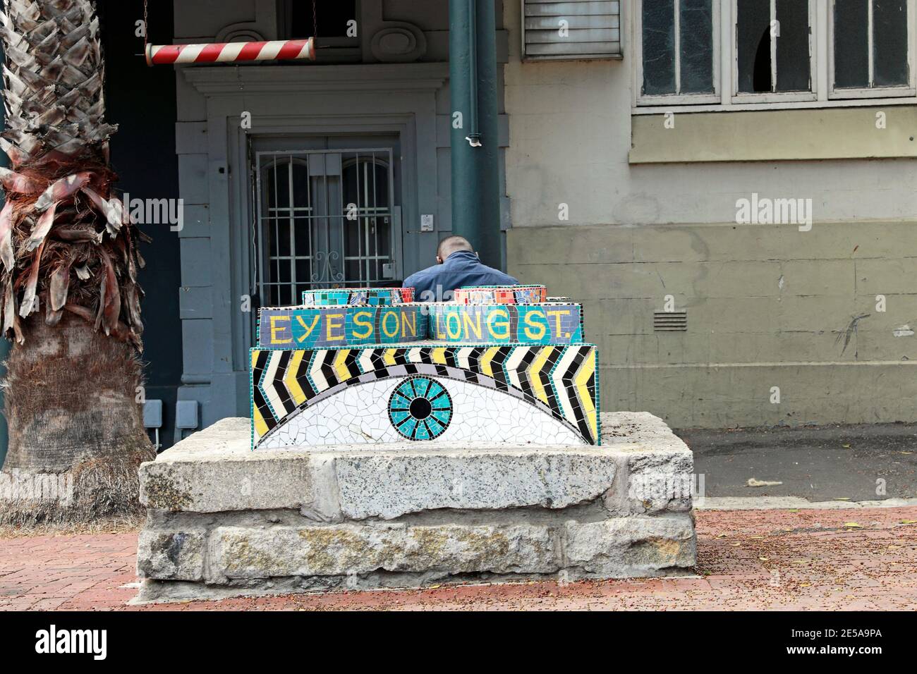 Mann auf Steinbank mit 'Eyes on Longstreet' Mosaik in Long Street, Kapstadt, Südafrika. Stockfoto
