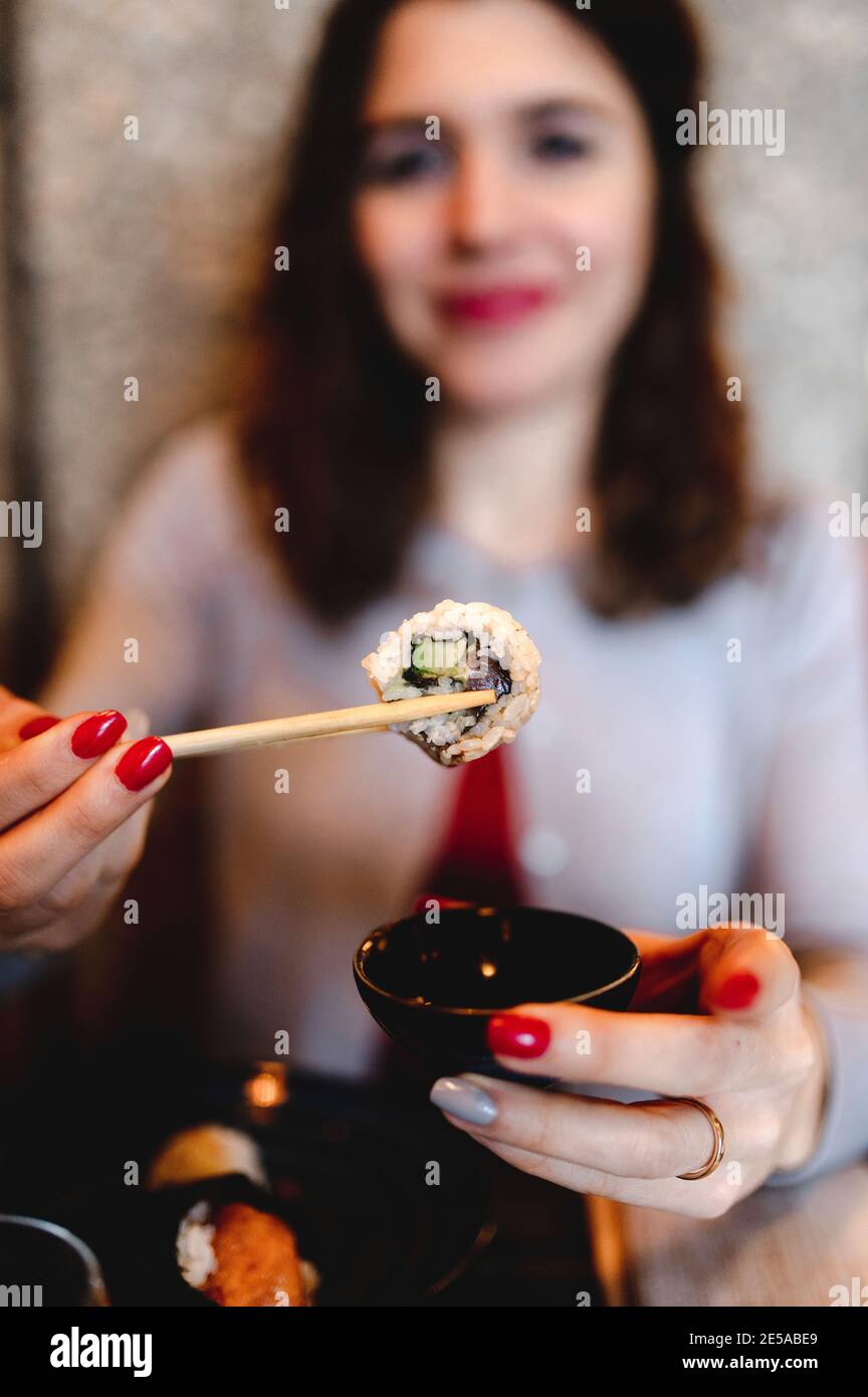 Flacher Fokus einer lächelnden lockigen Frau, die Sushi mit hält Essstäbchen Stockfoto