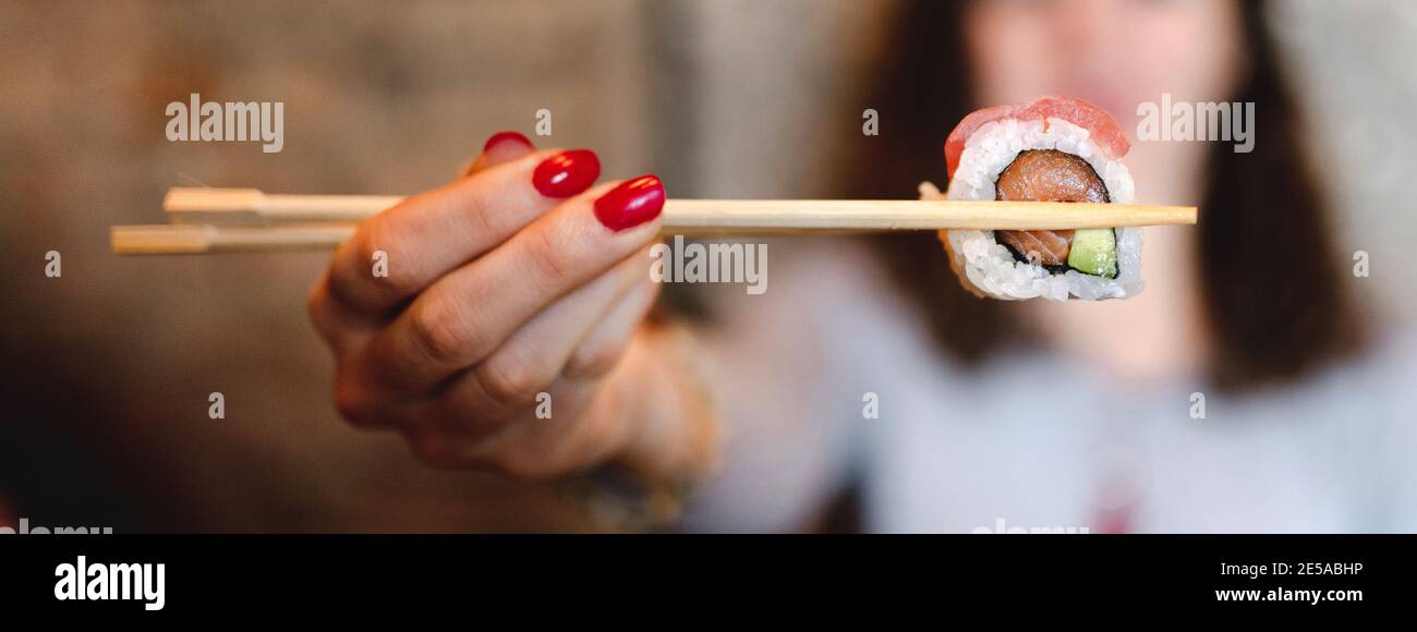 Selektiver Fokus einer Frau, die Sushi mit Essstäbchen hält Stockfoto