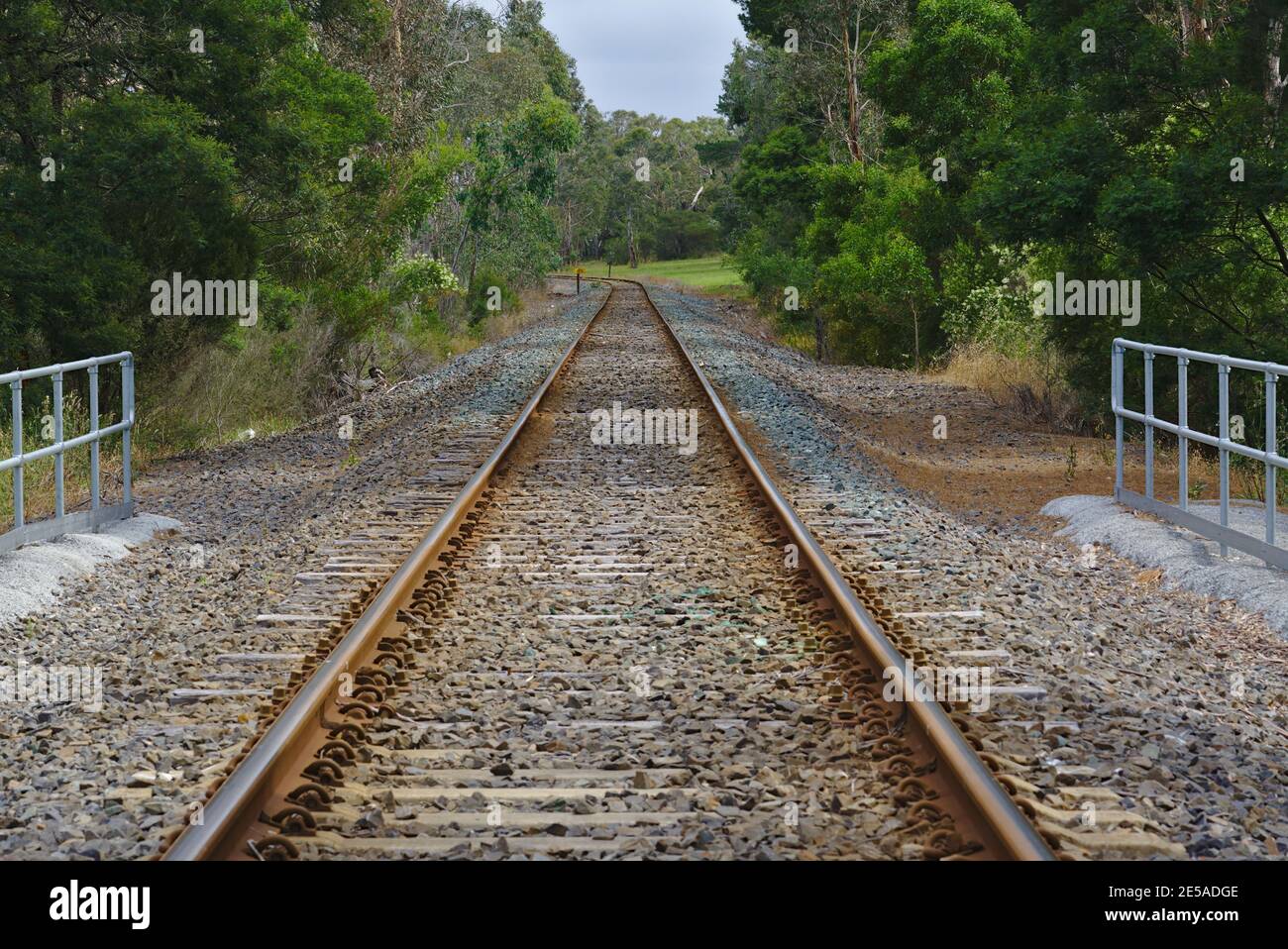 Leere Eisenbahn umgeben von grünen Bäumen und Kieselsteinen auf dem Boden Stockfoto