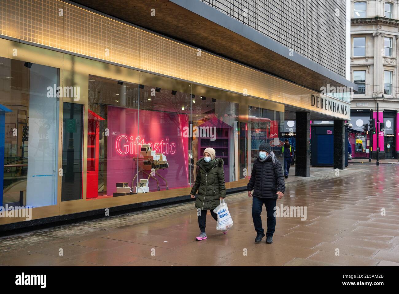 Zwei Menschen tragen Gesichtsmasken passieren den geschlossenen Debenhams Flagship-Store in der Oxford Street in London, die dauerhaft geschlossen ist, nachdem Online-Mode-Händler Boohookaufte die Debenhams Marke und Website für £55 Millionen in einem Deal, der den gleichnamigen Kaufhaus Namen überleben sehen wird, Aber die restlichen 118 Geschäfte des Unternehmens schließen für immer. Bilddatum: Mittwoch, 27. Januar 2021. Stockfoto