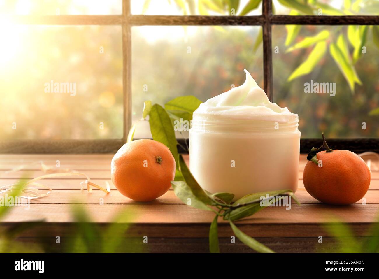 Natürliche Hautcreme mit Mandarinenextrakt mit Früchten und Blättern auf Holztisch. Vorderansicht. Stockfoto