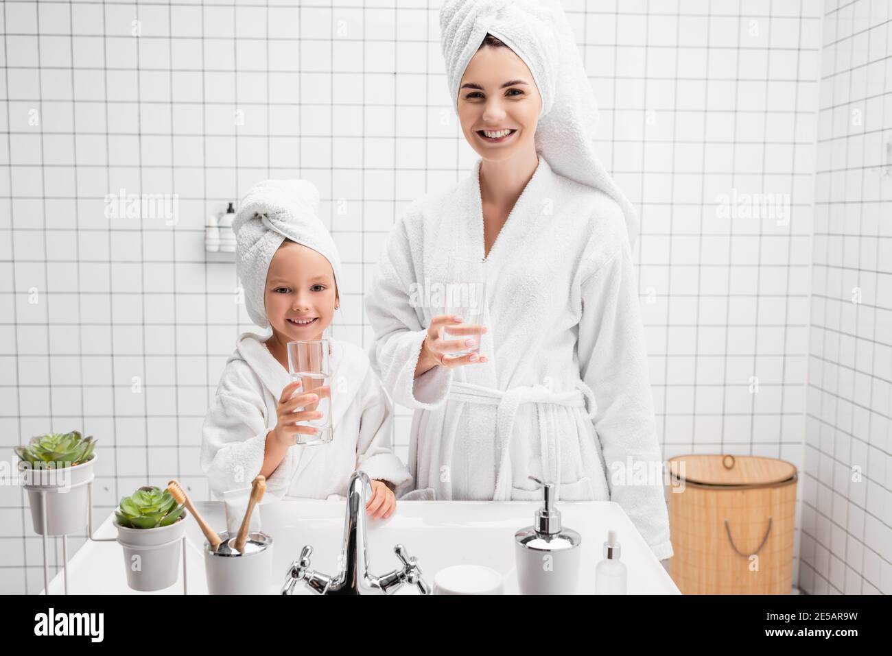 Positive Mutter und Tochter halten Gläser Wasser im Badezimmer Stockfoto