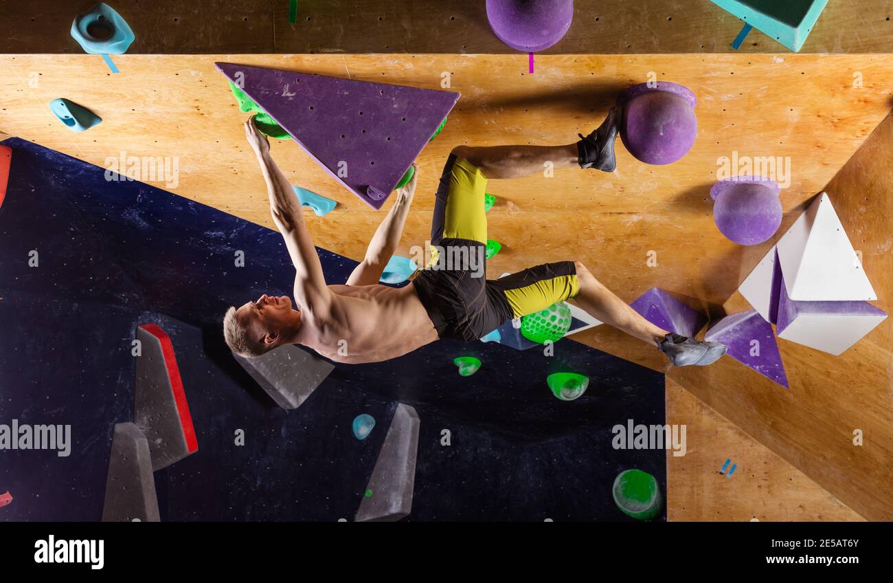 Junger Mann Bouldern in der Kletterhalle, versuchend, schwieriges Problem zu lösen Stockfoto