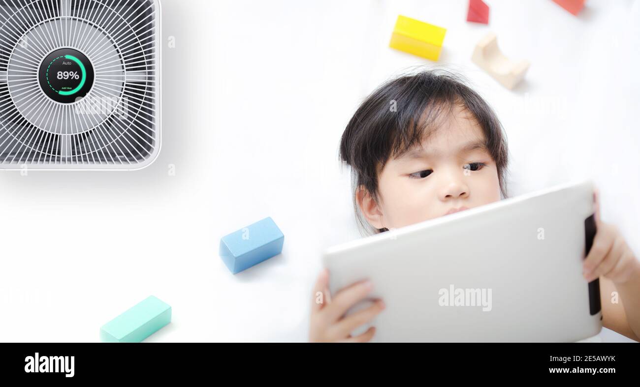 Kleines Mädchen mit Tablet im Zimmer mit modernen Luftreiniger Stockfoto