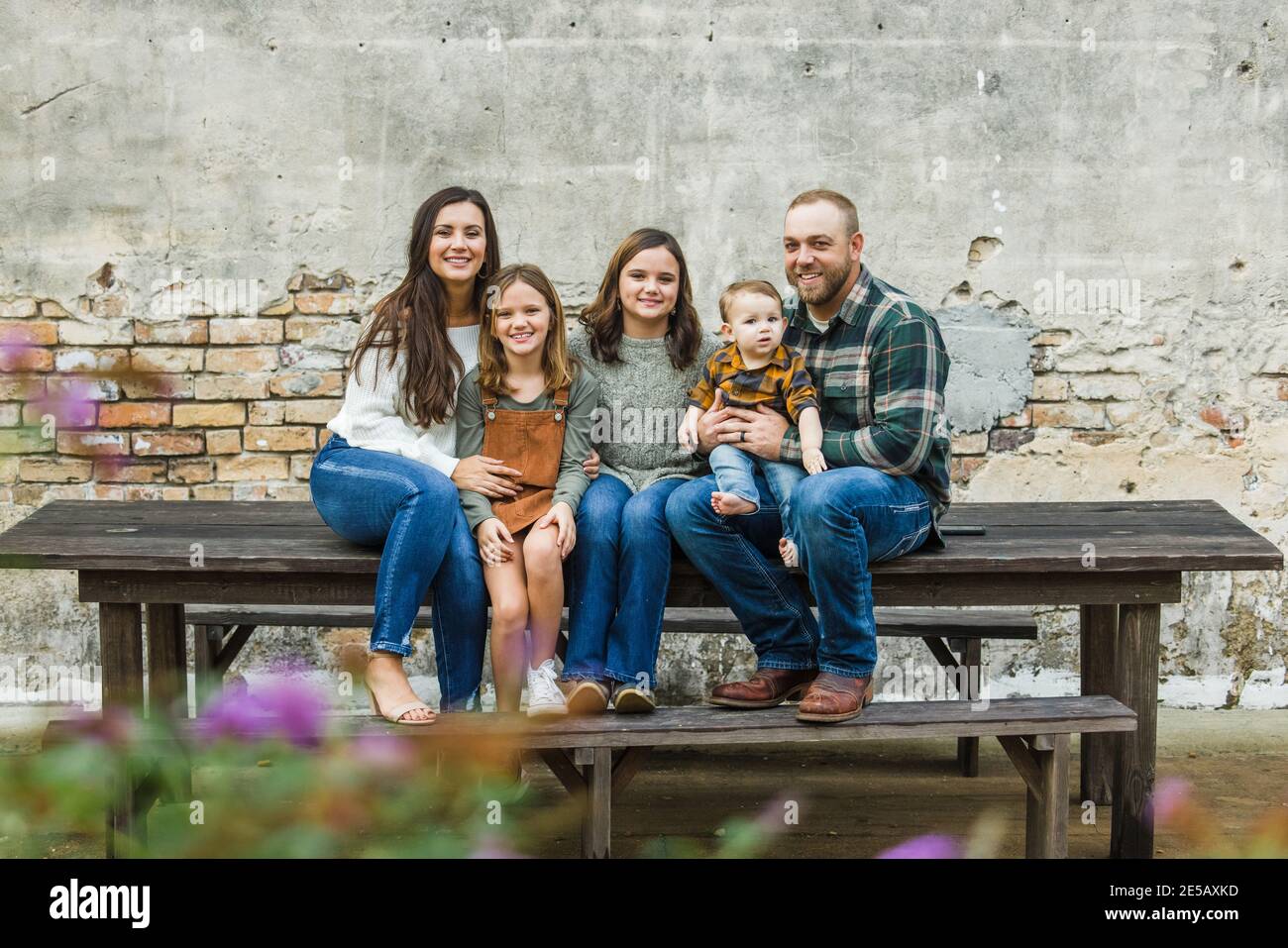 Blended Familie von fünf mit zwei Mädchen und ein Baby Junge sitzt auf einem Tisch an einem urban alten Backstein Wand Stockfoto